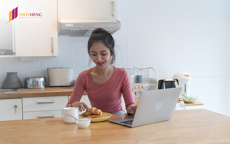 Woman enjoying a delicious pastry delivery at home while using a laptop